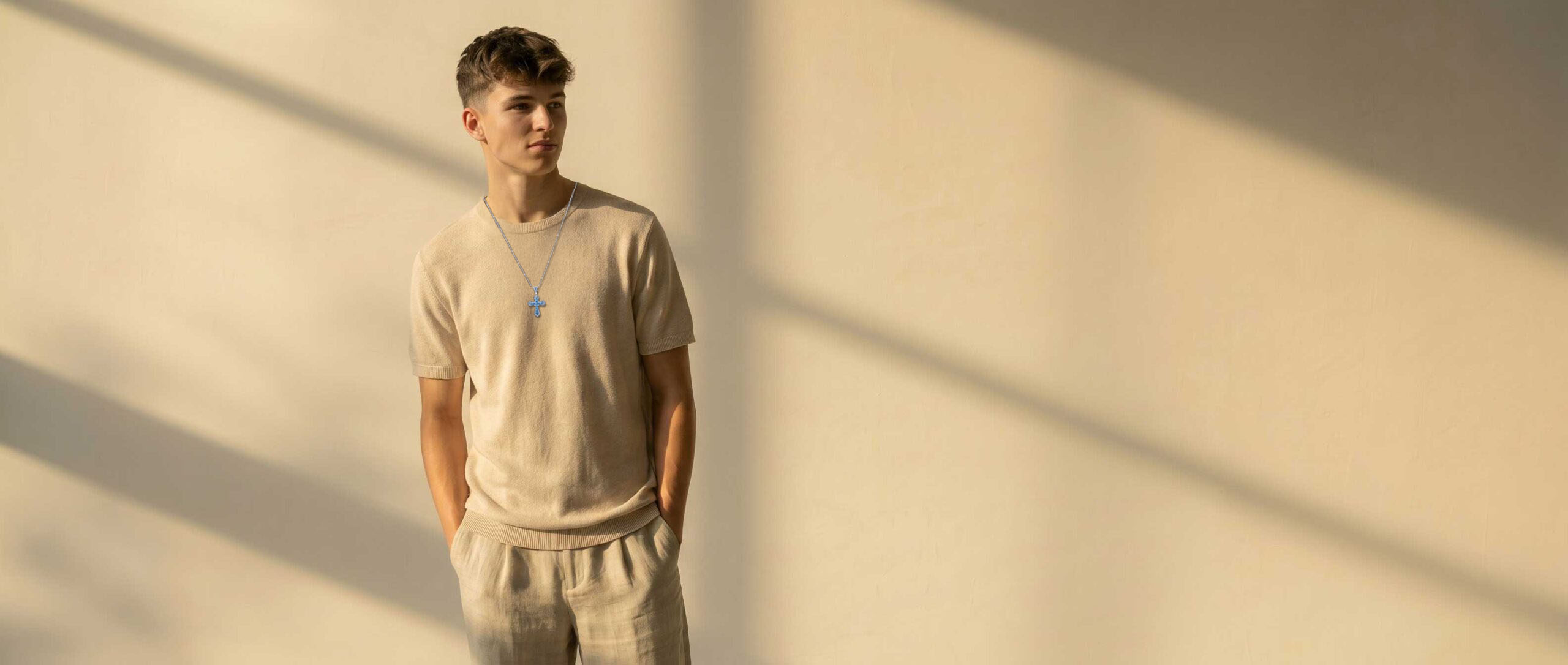 Bild eines jungen Mannes mit beigem T-Shirt und einer kette mit blauem Kreuzanhänger.