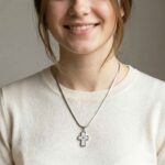 Lächelnde junge Frau trägt eine silberne Halskette mit weißem Kreuzanhänger um den Hals.