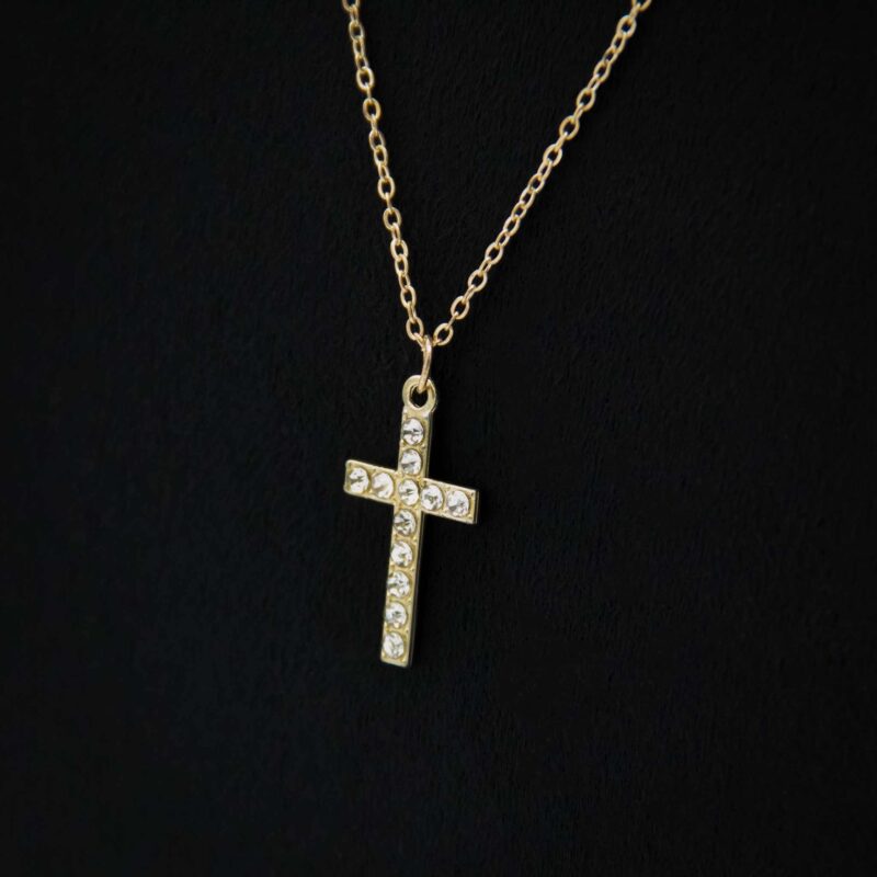Detailaufnahme eines funkelnden Kreuzanhängers an einer golden Halskette.